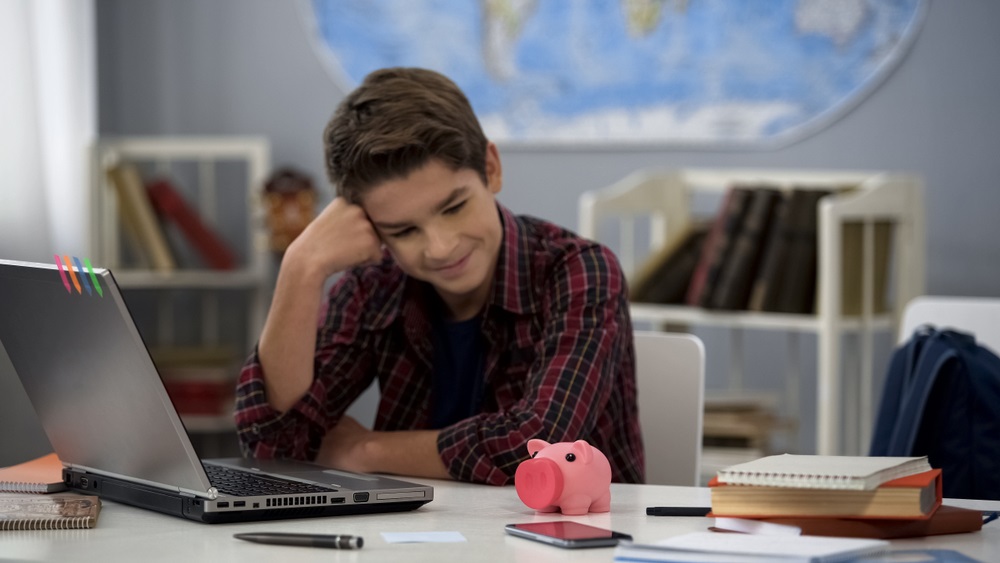 Teenager looking at piggybank on table sitting home, dreaming purchase, budget 