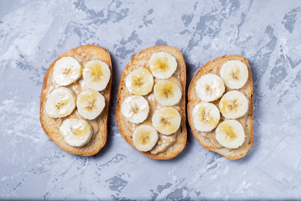 Delicious toasted sandwich bread with peanut butter, banana, honey, chia seeds on concrete background. Healthy, balanced traditional American school breakfast